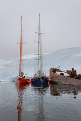 Two sailing yachts in the antarctic sea moored to rusty wreck