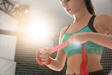 Young female boxer applying wrist wraps in gym