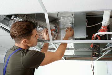 Male technician repairing industrial air conditioner indoors