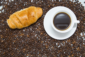 Coffee cup with croissant and coffee beans on wooden background. Top view, copyspace
