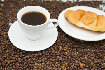 Coffee cup with croissant and coffee beans on wooden background. Top view, copyspace