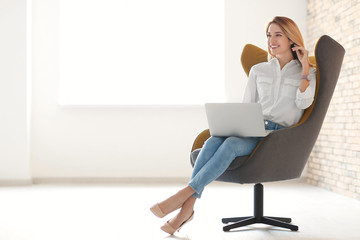 Young woman with laptop sitting in armchair indoors - Powered by Adobe