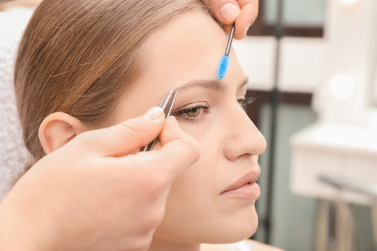 Young woman undergoing eyebrow correction procedure in salon