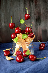 Cherries falling into waffle cones on dark wooden background