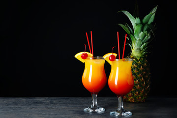 Glasses of Sex on the Beach cocktail and fresh pineapple on table against dark background