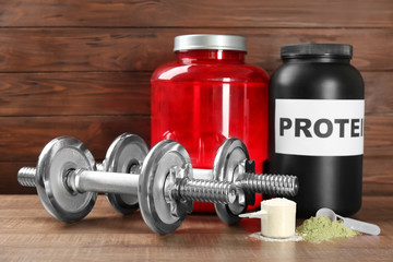 Composition with protein powder and dumbbells on wooden background