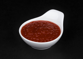Tomato paste in white bowl on black background