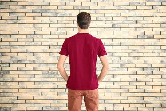 Young man in stylish t-shirt against brick wall. Mockup for design