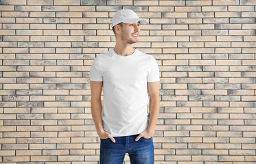 Young man in stylish t-shirt against brick wall. Mockup for design