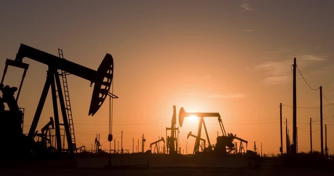 The sun rises behind a large oil field.