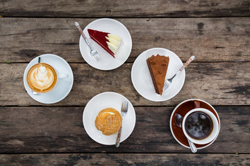 Close-up of Shu cream (Japanese cream puff), red velvet cake, chocolate cake, and hot coffee on wooden table in outdoor garden. Concept sweets enjoy eating.