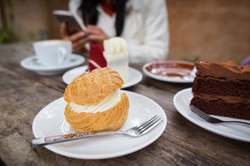 Close-up of Shu cream (Japanese cream puff), red velvet cake, chocolate cake, and hot coffee on wooden table in outdoor garden. Concept sweets enjoy eating.