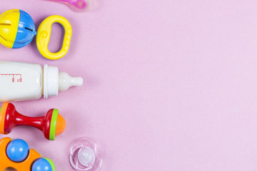 Baby accessories. Wooden toys, pacifier and bottle on Pink background top view copyspace
