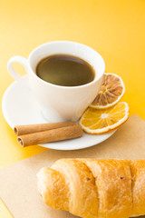 I love coffee concept. Coffee cup, croissant and sun dried orange on yellow background