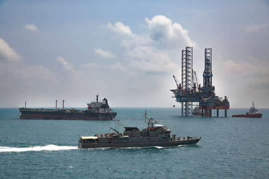 Military navy ships in a sea bay with oil rig background