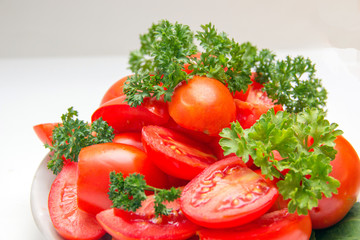 Slices of red ripe tomato and fresh herbs on a plate in the kitchen. Natural authentic still lifes, white back