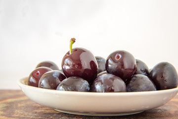Fresh plums in plate with waterdrops on white background