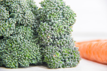 Fresh broccoli sprouts florets with tiny waterdrops with orange carrot blured on white background, close-up macro shot, healthy diet concept