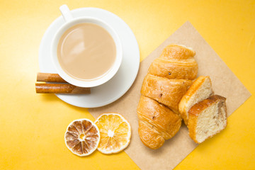 I love coffee concept. Coffee cup, croissant and sun dried orange on yellow background. Closeup and top view