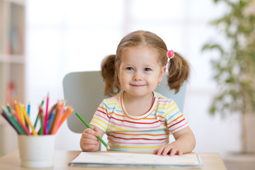 Cute happy little child girl drawing with pencils in daycare center