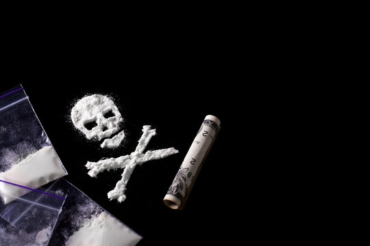 Drug dependence Kills. A line of cocaine in the form of a skull and a roll of a dollar, sachets with a dose. Black background. Addiction concept. Copy space for text