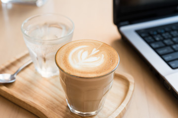 coffee cup latte art with cake and laptop computer on a wooden table in a coffee shop.