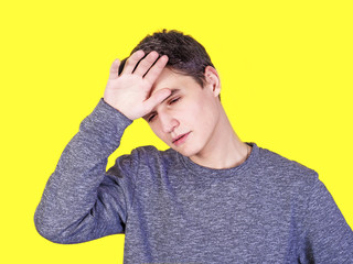 A tired man stressed sweating with a headache fever isolated against a yellow wall background. The troubled guy wipes the sweat on his face