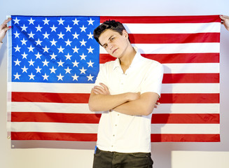 Young confident man in white shirt with arms crossed, standing against US flag background who hold two hands
