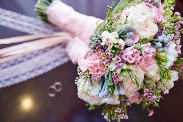 Fototapeta premium Beautiful bridal bouquet and engagement rings in blur, selective focus. Wedding bouquet and rings, copy space. Wedding concept