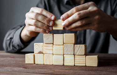Businessman building a pyramid with empty wooden cubes. Concept of business hierarchy and business...