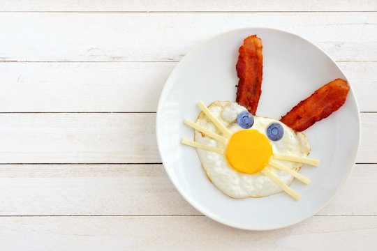 Easter breakfast with cute bunny face made of egg and bacon. On white plate against a white wood background.