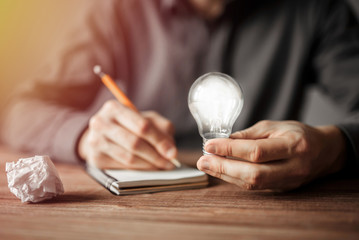 Businessman holding light bulb and writing down in the notebook new creative ideas. Concept of innovative technology and creativity.
