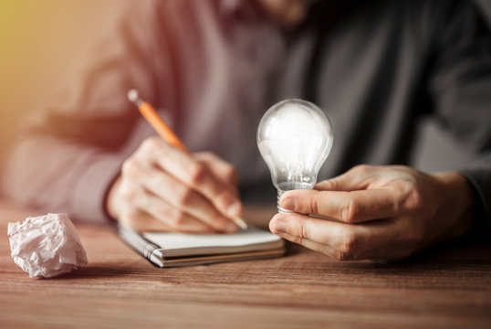 Businessman holding light bulb and writing down in the notebook new creative ideas. Concept of innovative technology and creativity.