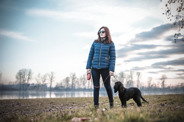 Woman and dog standing by the river. Beautiful sky in background.