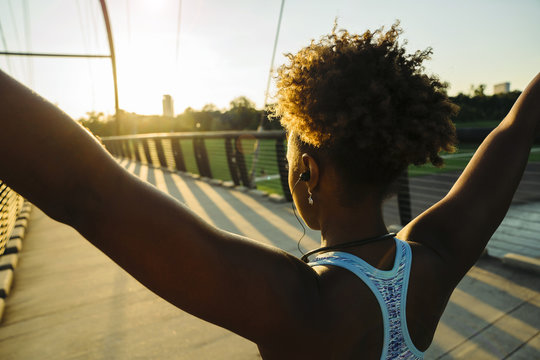 Mixed Race woman wearing earbuds stretching arms on bridge