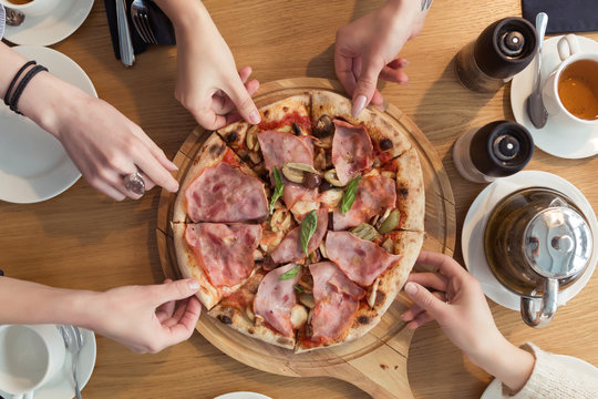 Top view of women hands take slices of pizza with different toppings on a wooden table. Friends meeting at italian cafe or restaurant