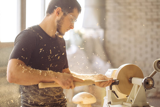 Young carpenter processing wooden plank on special woodworking machine - Powered by Adobe