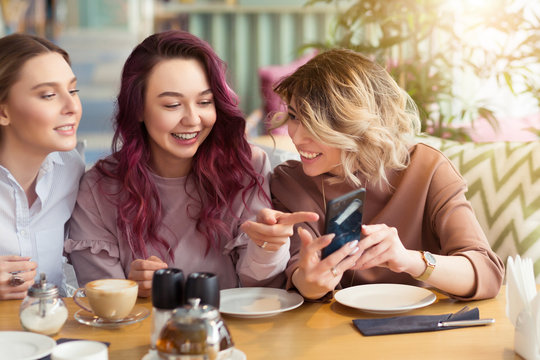 Young beautiful girls taking selfie photo at cafe or coffee shop. Happy women friends having fun, talking together and looking photos at mobile phone. Female friendship, communication concept