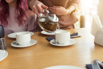 A woman's hand pours tea at white cup, holds a teapot in cafe or coffee shop