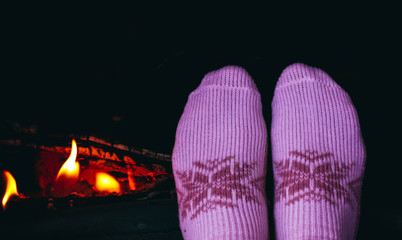 Burning wood at the fireplace, female legs in socks warming up. Firewood bricks at the fire, woman foot heating.