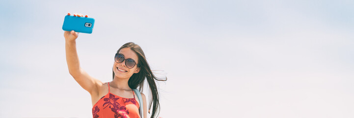 Selfie picture with phone woman tourist holding cellphone taking self-portrait photo on summer holiday. Young people lifestyle banner panorama with copy space on blue sky background.