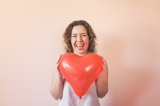 ​Beautiful curly young woman holding a heart shape air balloon on color background. Valentine's Day concept, symbol of love.