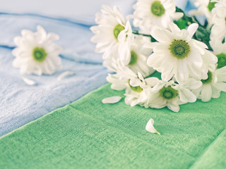Naklejka na ściany i meble A bouquet of white chrysanthemum is on a green linen fabric. Nearby is a blue tablecloth with a flower on it. Cozy home background