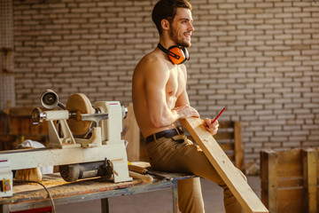 naked carpenter using straightedge to draw line on board.