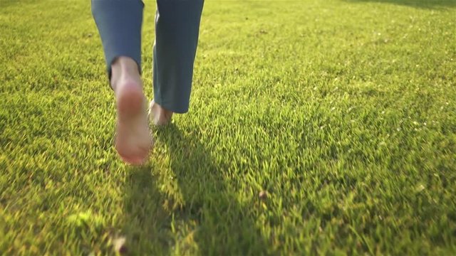 Rea view of an unrecognizable young woman walking on the grass barefoot. Concept of freedom and enjoying one s life. Tracking real time medium shot