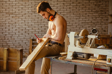 naked carpenter using straightedge to draw line on board.