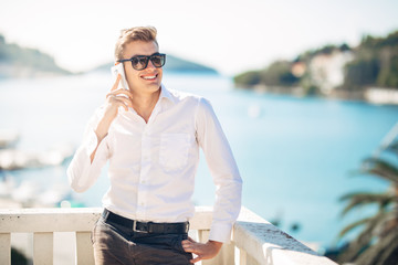 Fototapeta na wymiar Young handsome man enjoying stay at luxury resort hotel with panoramic view on the sea.Smiling business man using his smartphone options at a earned tropical vacation.Business traveling.Outsourcing