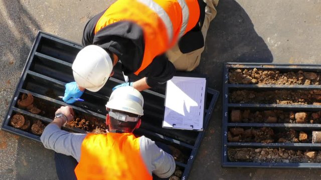 Drilling rig industry. Workers examining soil samples taken from long metal rotary pipe and writing down the dates for further science explorations. Energy and power