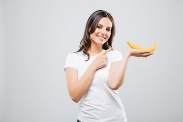 closeup portrait of attractive caucasian smiling woman brunette pointed on bananas isolated on white background. Healthy food concept. Skin care and beauty. Vitamins and minerals.