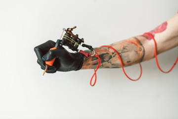 Man's hand holding tattoo machine on white background. the red wires
